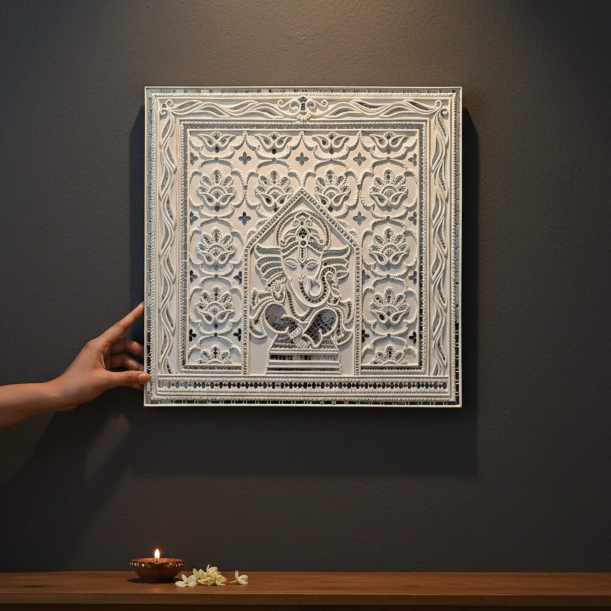 2ft Ganesha White Lippan wall art with intricate design on a dark wall, hand holding it.
