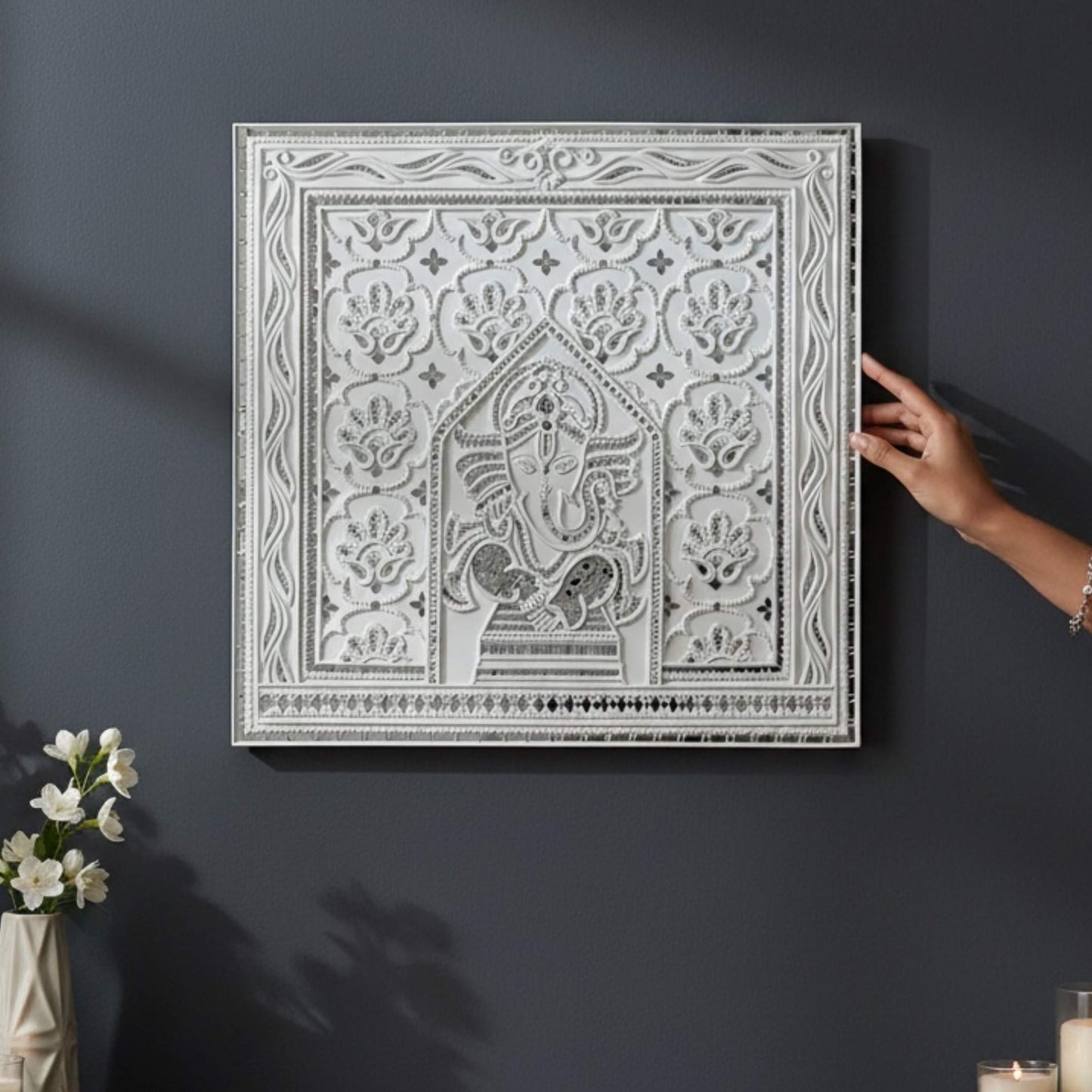 2ft Ganesha White Lippan wall art with intricate patterns on a dark wall, accompanied by a hand and flowers.