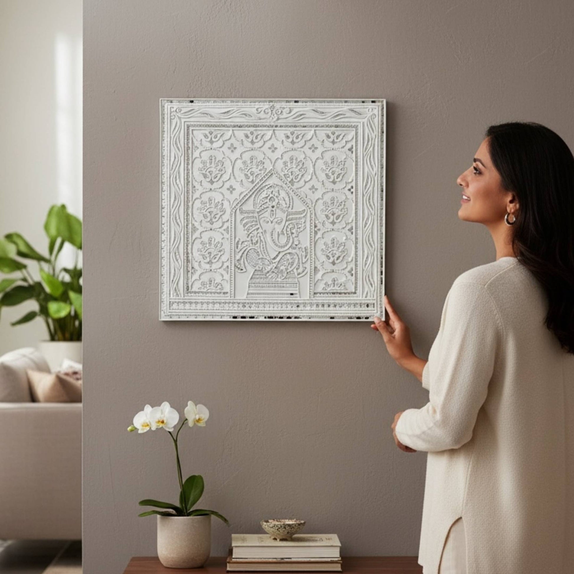 Woman adjusting 2ft Ganesha White Lippan in a living room.