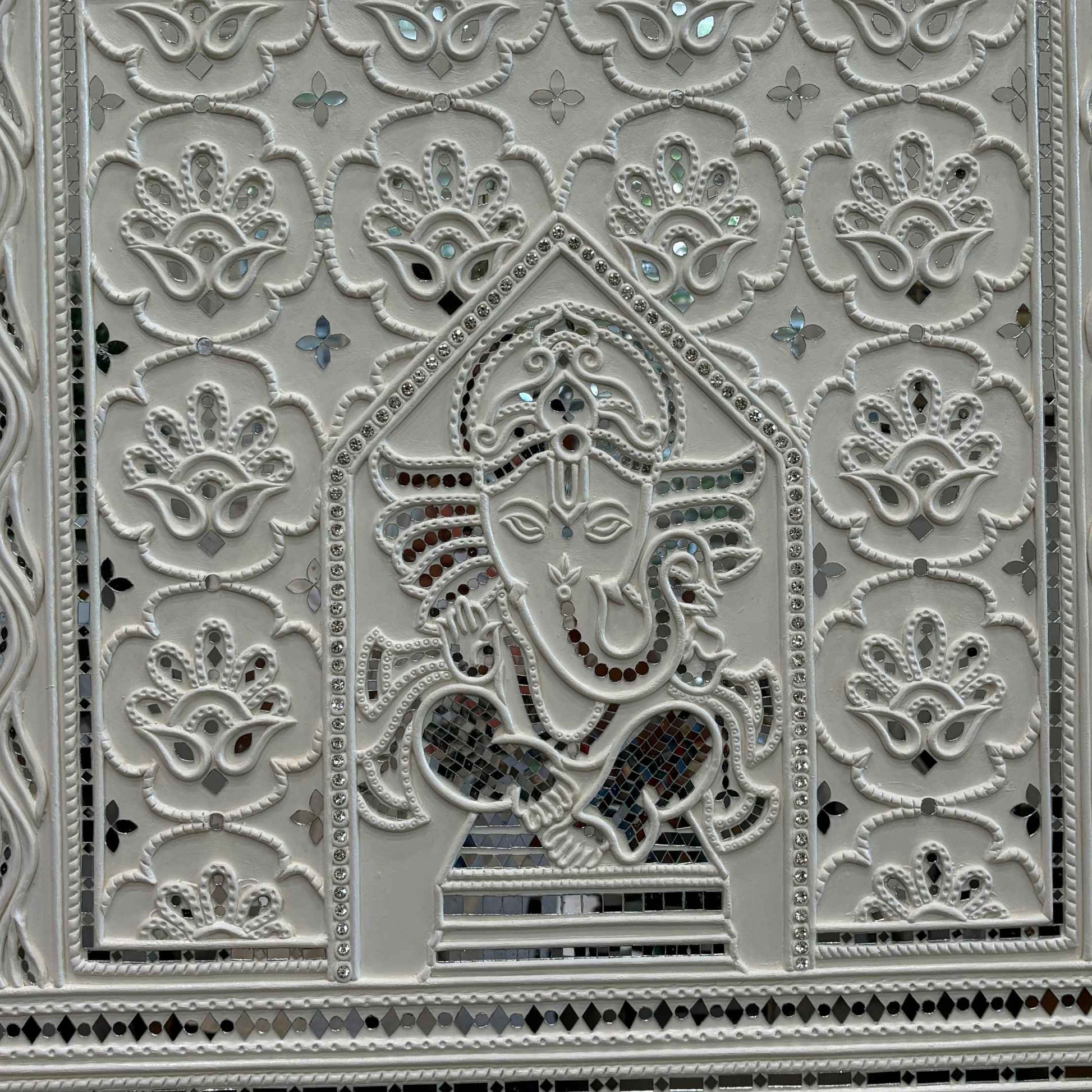 Decorative panel with intricate patterns and a central figure, likely a deity, on a white background.