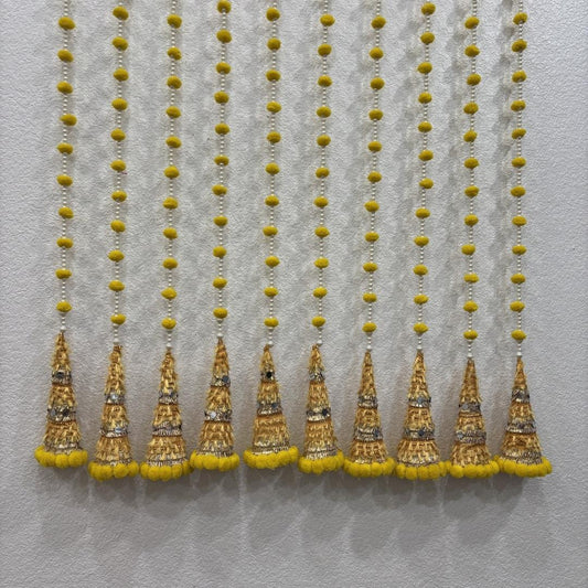 Ten yellow woolen bead strings end in gold-embroidered gota cone tassels with pompom trim on a wall.