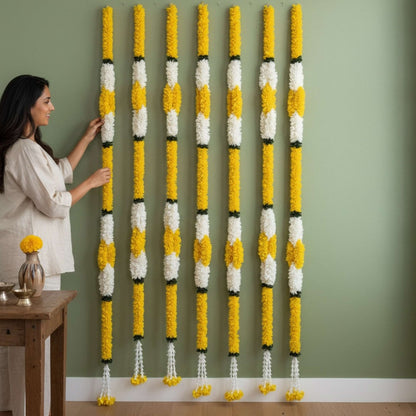 Woman arranging fabric marigold jasmine garlands on green wall Indian housewarming decor
