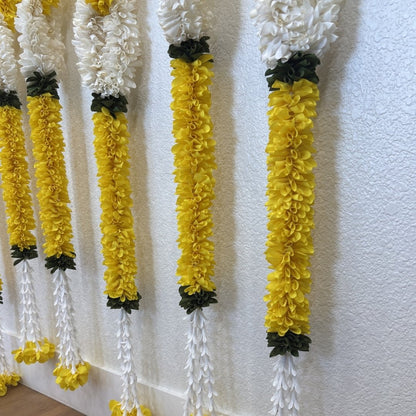 Yellow and white flower garlands hanging vertically against a textured off-white wall.