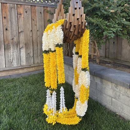 Fabric marigold jasmine garlands draped over wooden urli outdoor Indian wedding decor