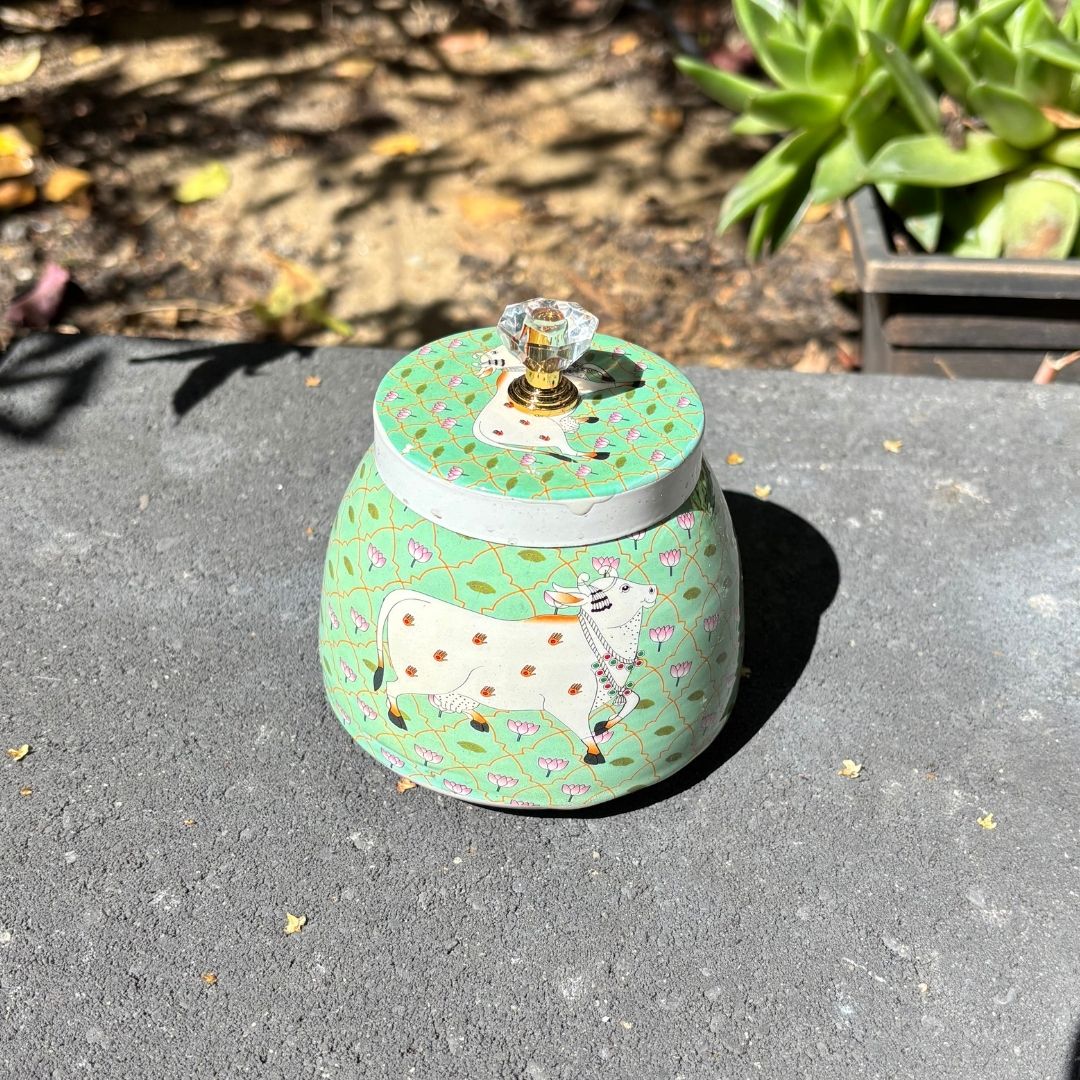 Decorative jar with a cow design on a gray surface outdoors