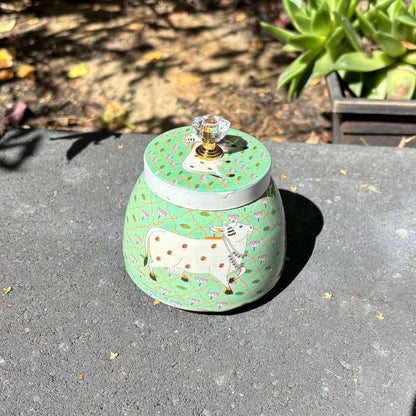 Decorative jar with a cow design on a gray surface outdoors