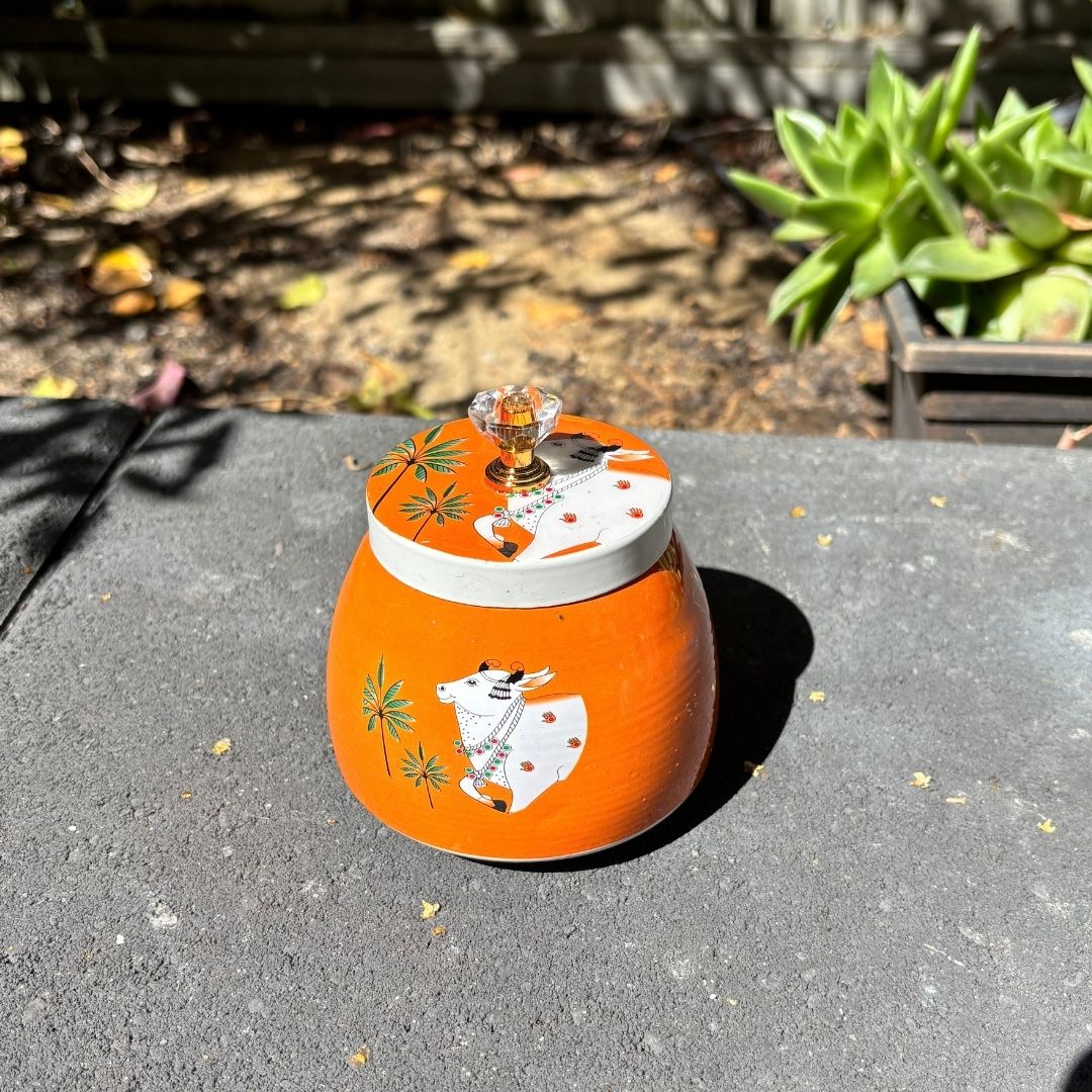 Orange metal container with a lid featuring a design on a concrete surface.
