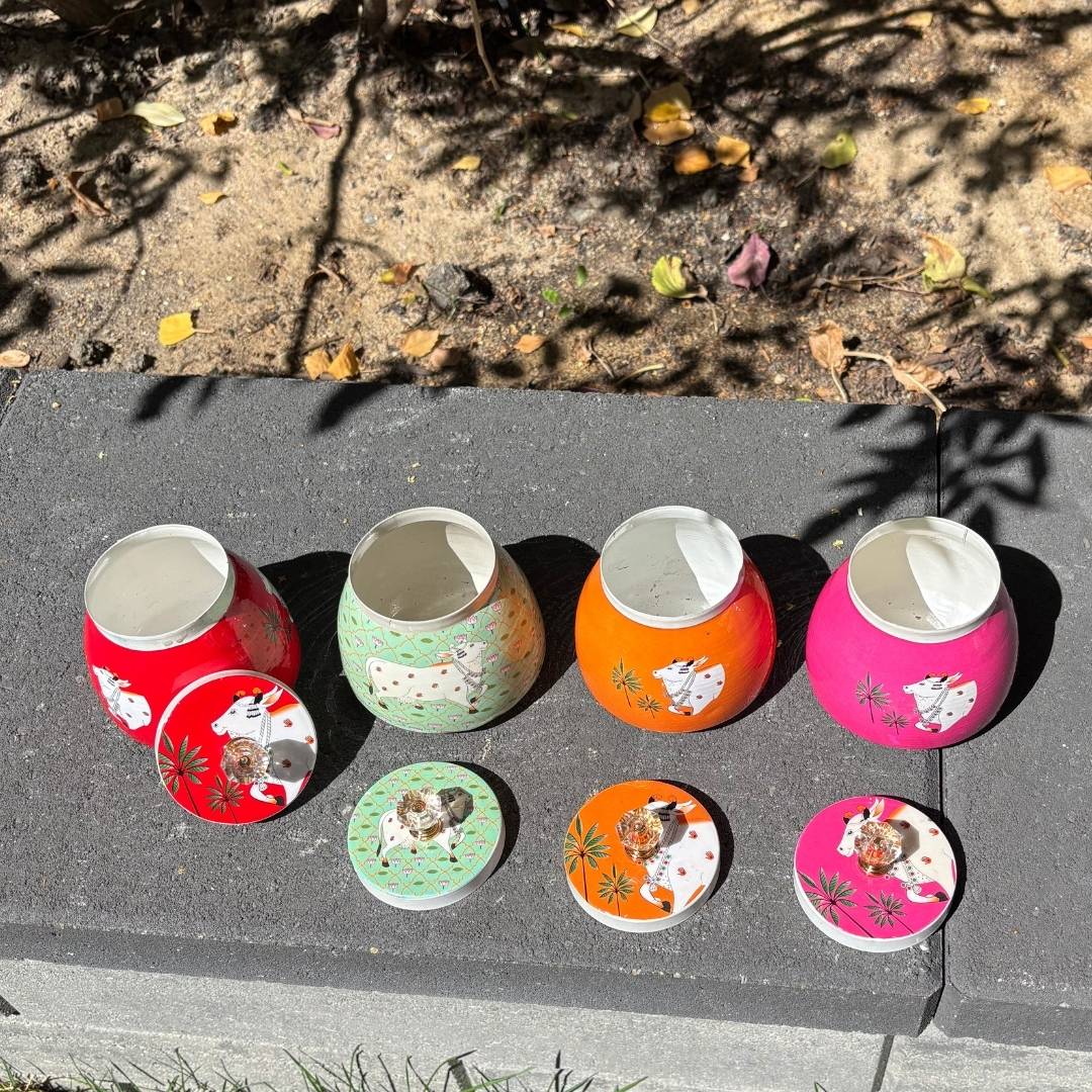 Set of colorful small containers with decorative lids on a stone surface.
