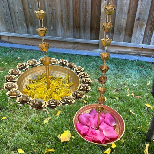 Rose and Hammered Urlis from Urli Utsav, hanged in backyard for festive diwali decoration - Decorative outdoor setup with gold floral arrangements and bowls of yellow and pink flowers on grass.