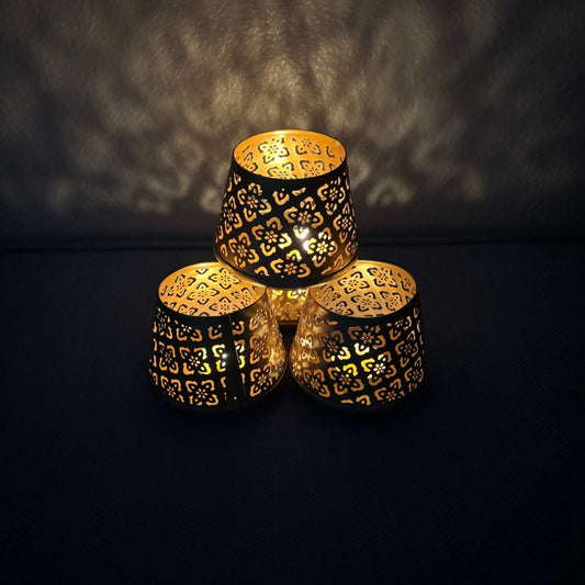 Four ornate, patterned metal candle holders stacked on a dark background