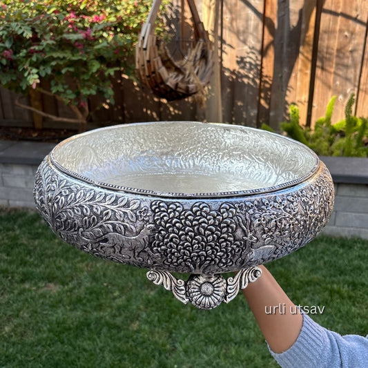 Jungle theme german silver urli bowl held by a person outdoors with greenery in the background