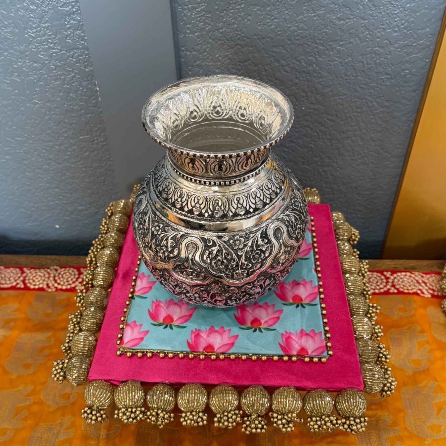 7-Inches Antique Silver Lota or Kalash on a colorful fabric with a gold border against a blue wall.