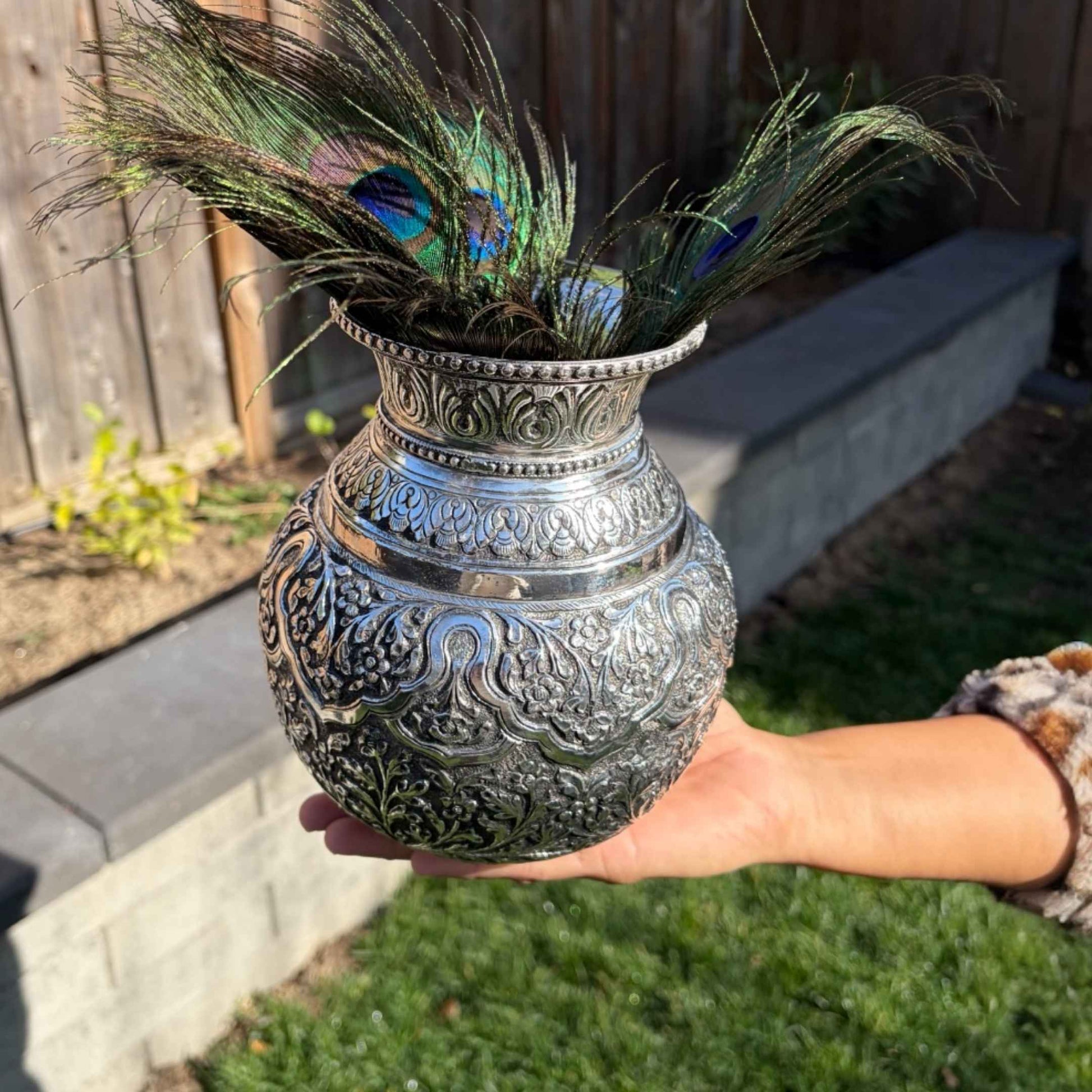 7-Inches Antique Silver Lota or Kalash with peacock feathers held by a person outdoors.