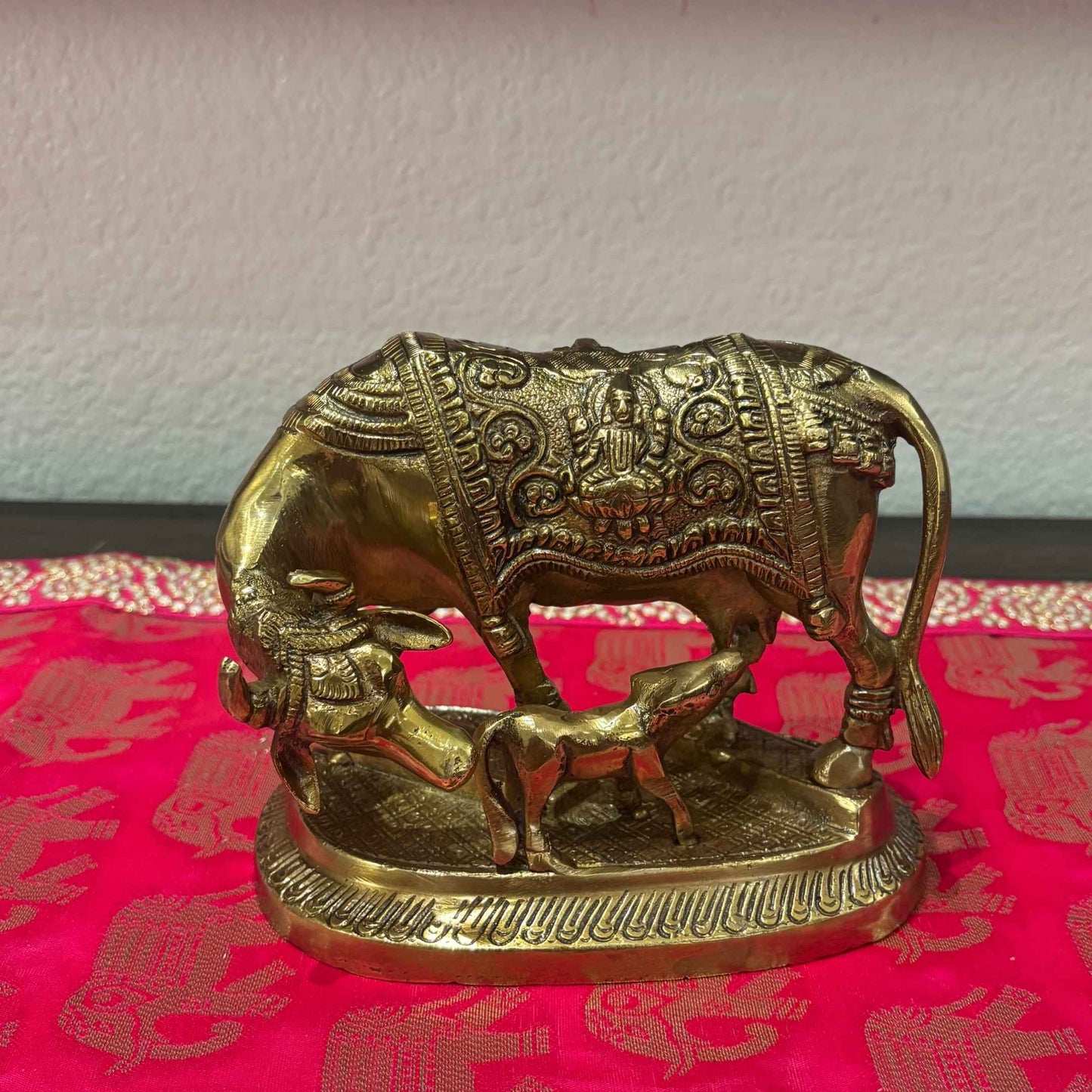 Antique gold Brass Kamdhenu Cow and Calf figurine displayed on red traditional fabric