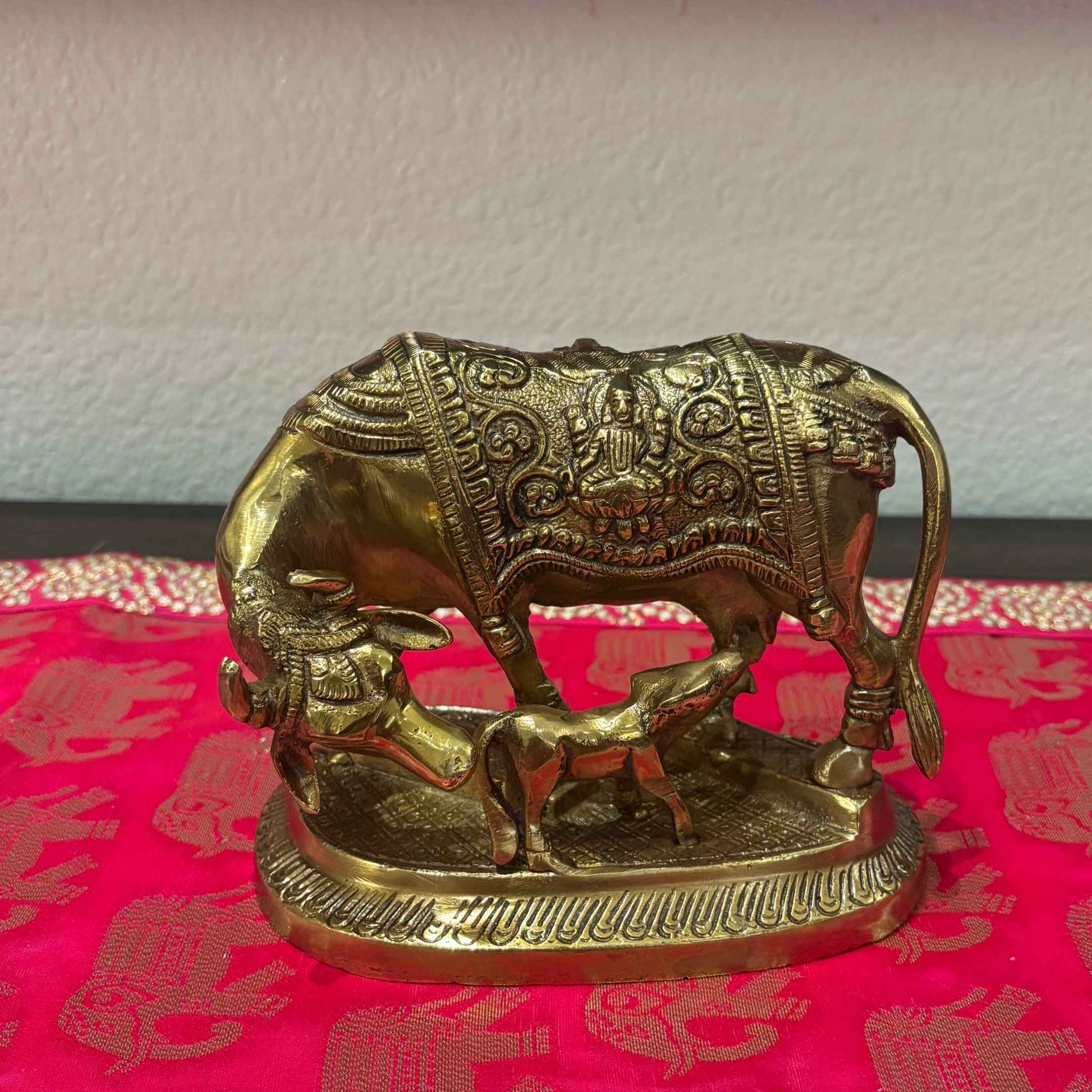 Antique gold Brass Kamdhenu Cow and Calf figurine displayed on red traditional fabric