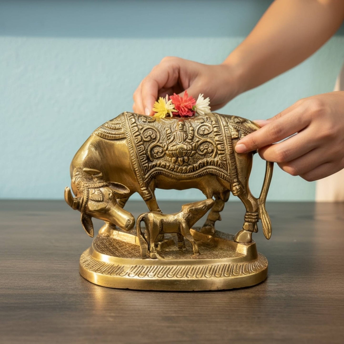 Hands placing a flower on Brass Kamdhenu Cow idol, symbol of prosperity and blessings