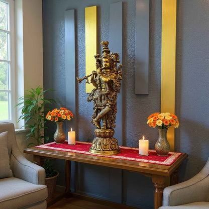 Brass Krishna statue styled on a wooden console table in a living room, with a red runner, candles and flower arrangements against a blue wall with gold and gray panels