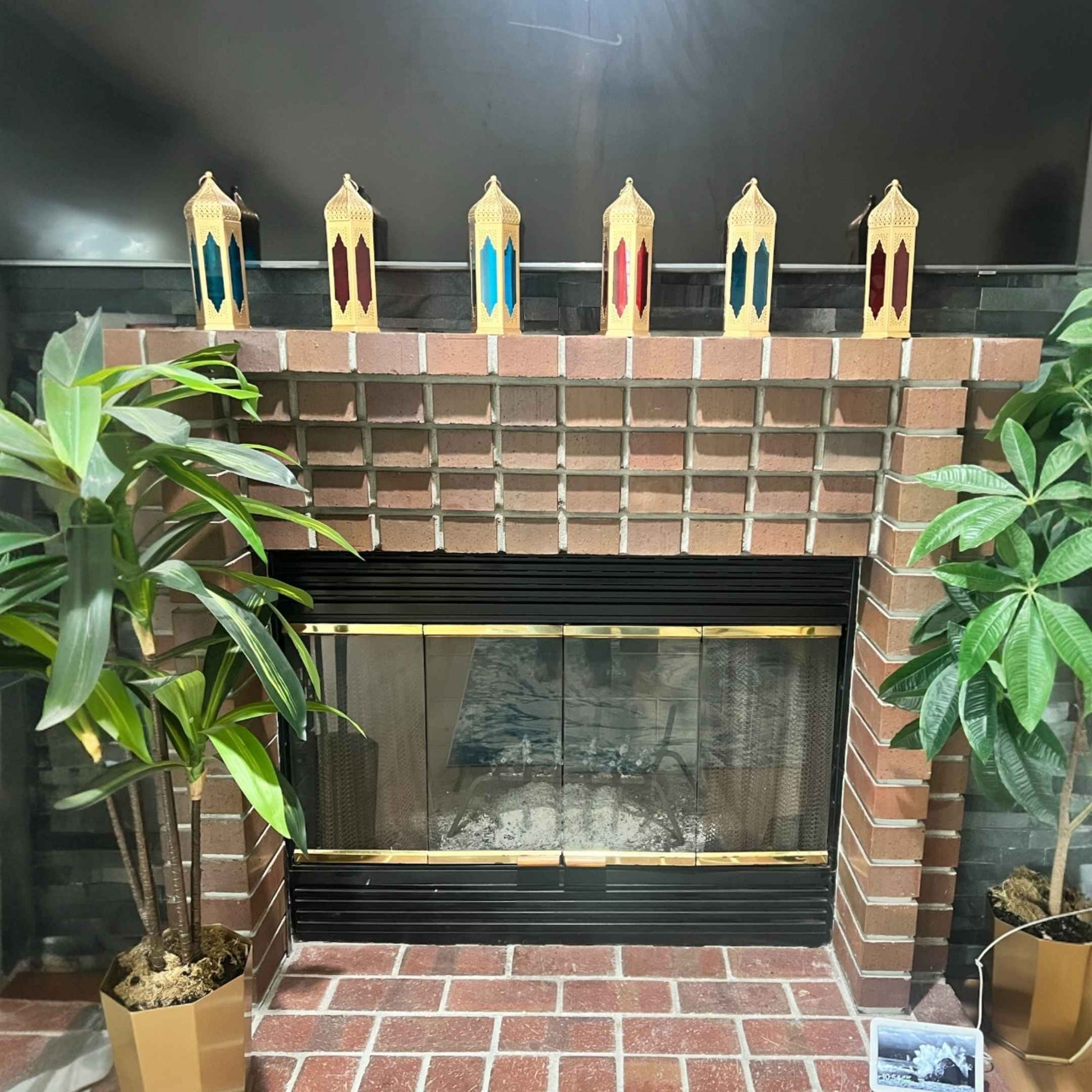 Interior setting featuring a Moroccan lantern with stained glass panels, placed near a brick fireplace, enhancing the ambiance with its warm glow.