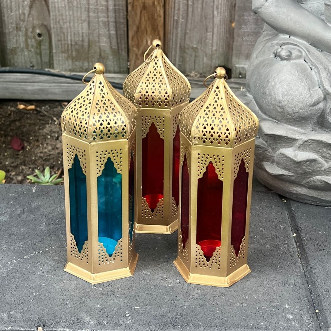 Set of three Moroccan-inspired lanterns with red and blue stained glass panels, arranged on a stone surface, showcasing their intricate design.