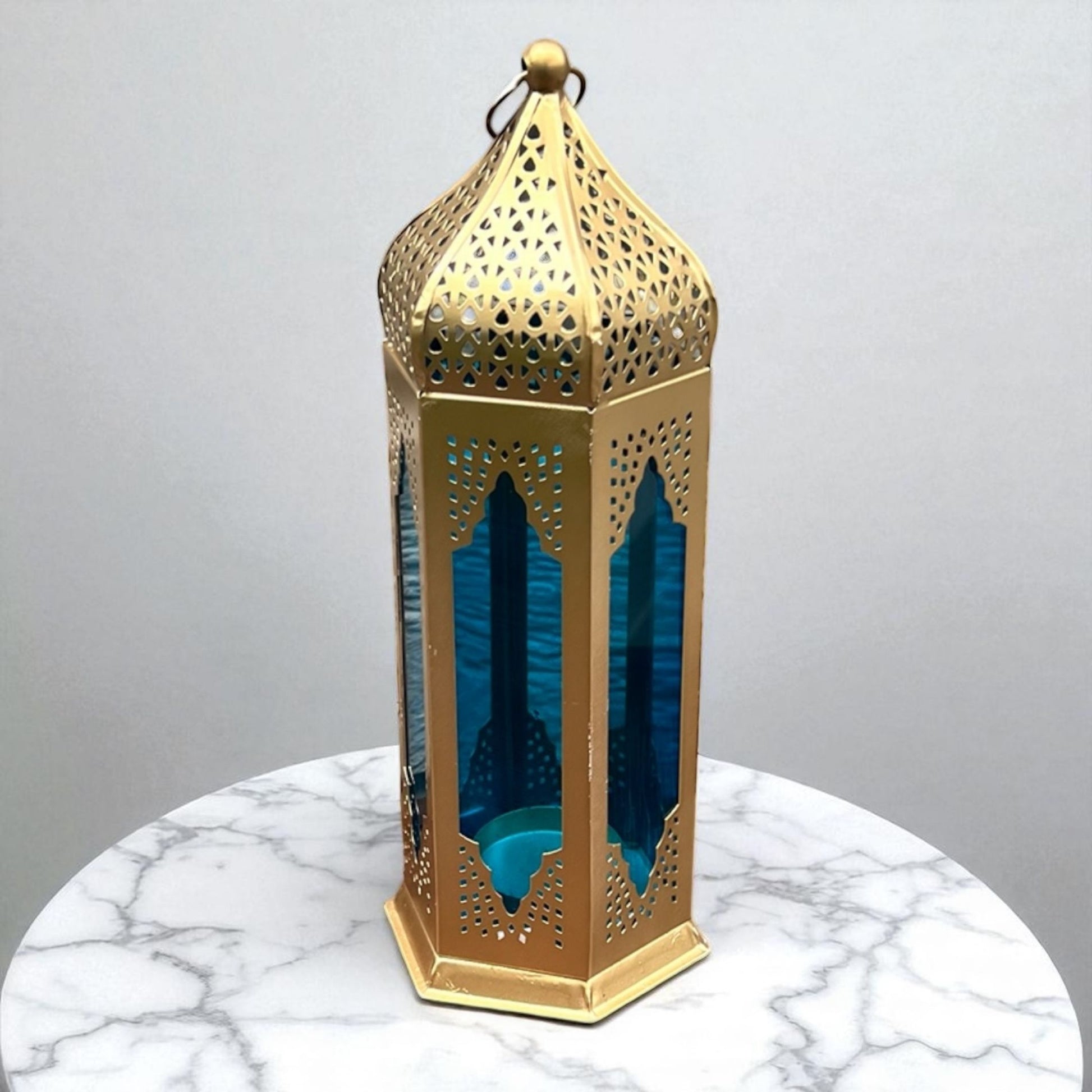 Close-up of a Moroccan tealight lantern with blue stained glass and gold metal accents, placed on a marble surface, showcasing its intricate design.