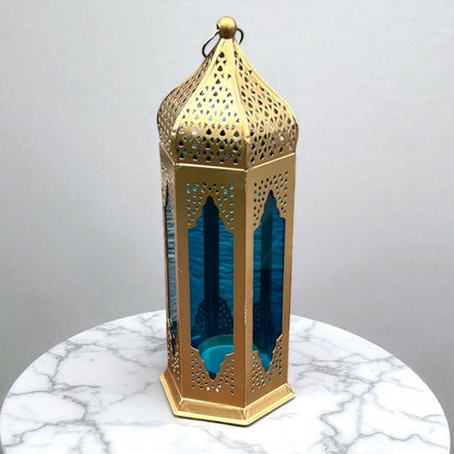Close-up of a Moroccan tealight lantern with blue stained glass and gold metal accents, placed on a marble surface, showcasing its intricate design.