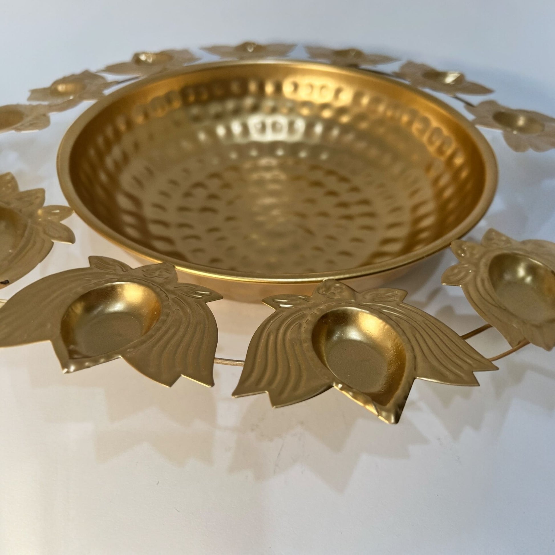 Close-up of the handmade hammered gold finish and intricate lotus petal rim on a metal urli.