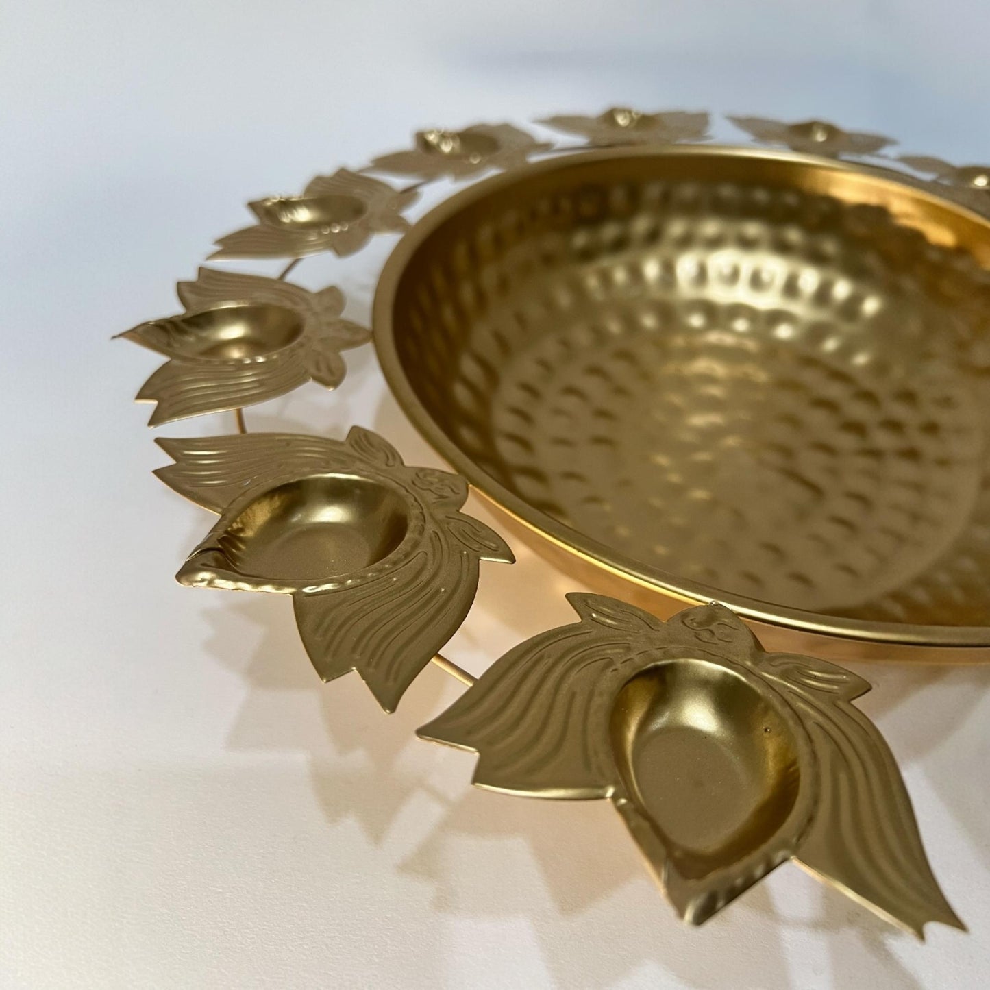 Close-up of the handmade hammered gold finish and intricate lotus petal rim on a metal urli.