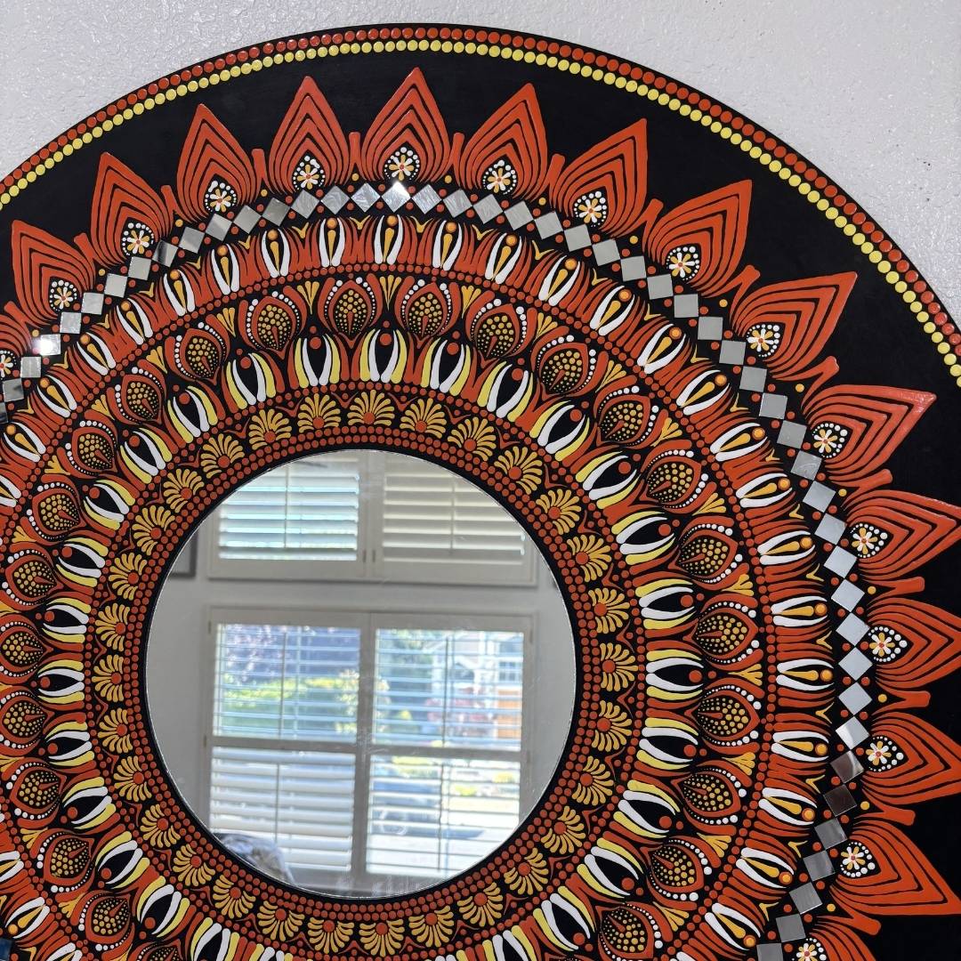 Round mandala mirror with intricate orange patterns hung on plain wall