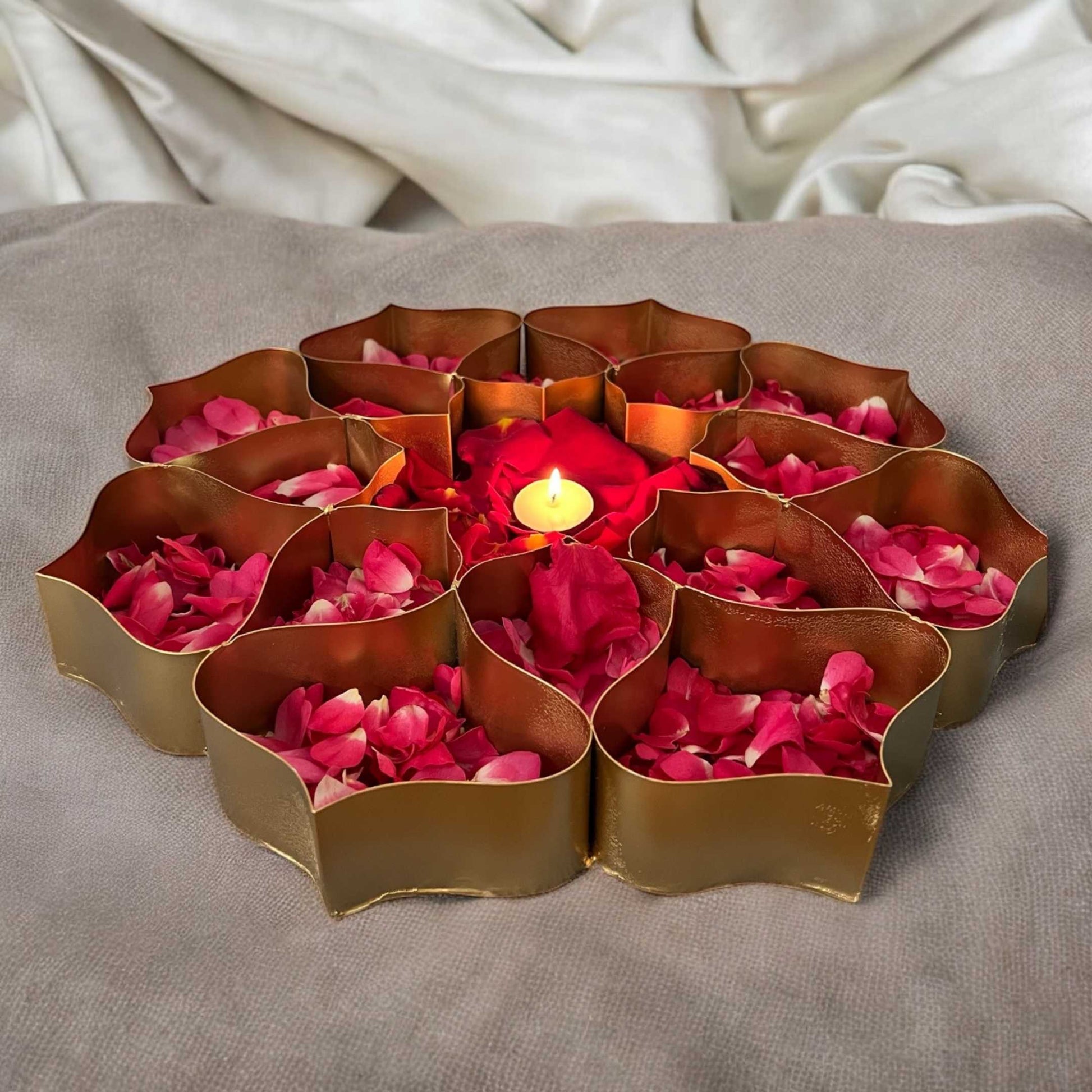 Decorative copper tray with red and pink rose petals and a lit candle on a gray surface.