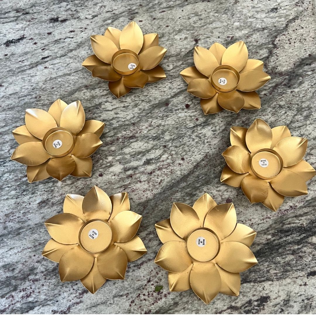 Six gold lotus t-light holders with unlit tea lights arranged on a gray granite surface