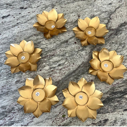 Six gold lotus t-light holders with unlit tea lights arranged on a gray granite surface