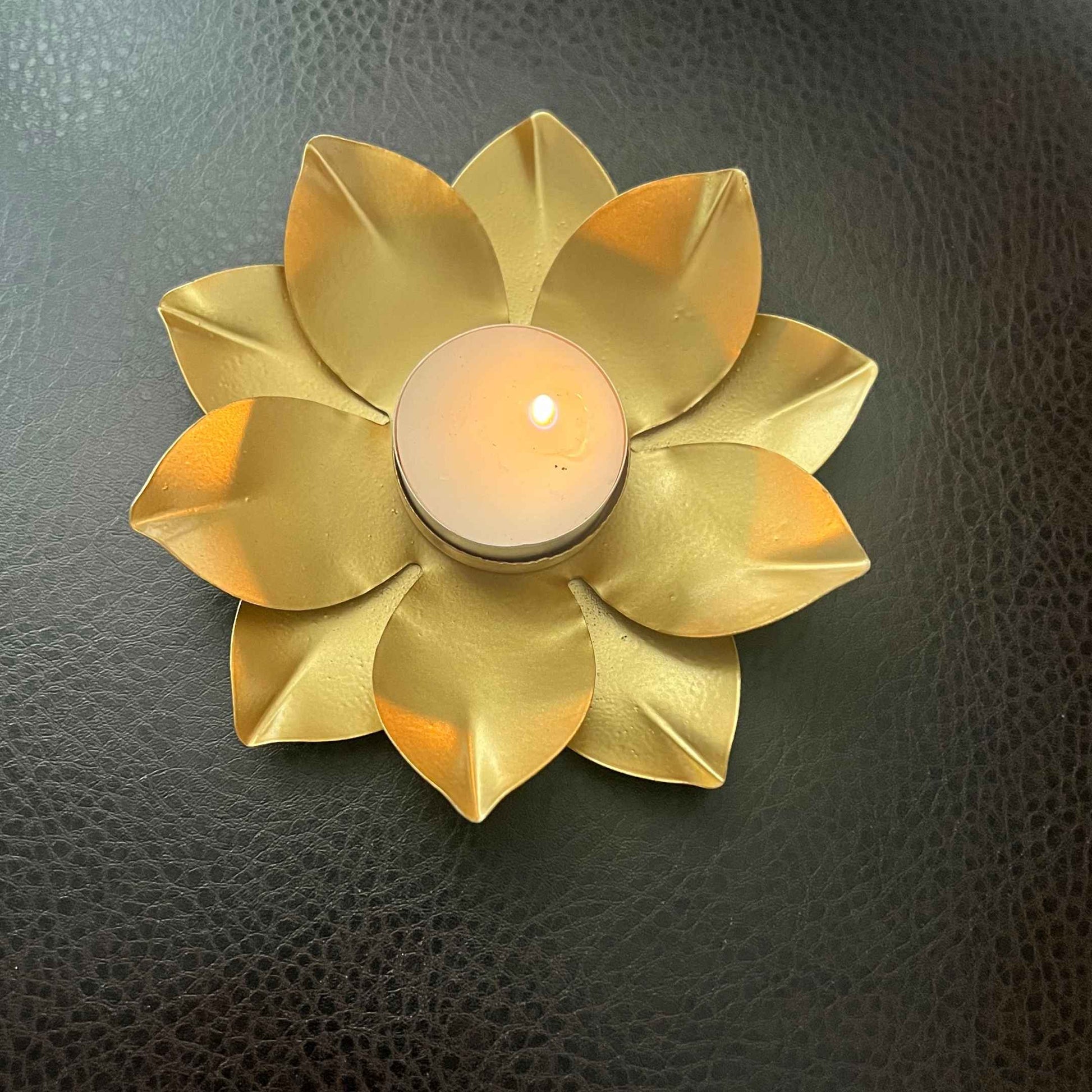 Close-up of a single gold lotus t-light holder with a lit tea light on a dark leather surface