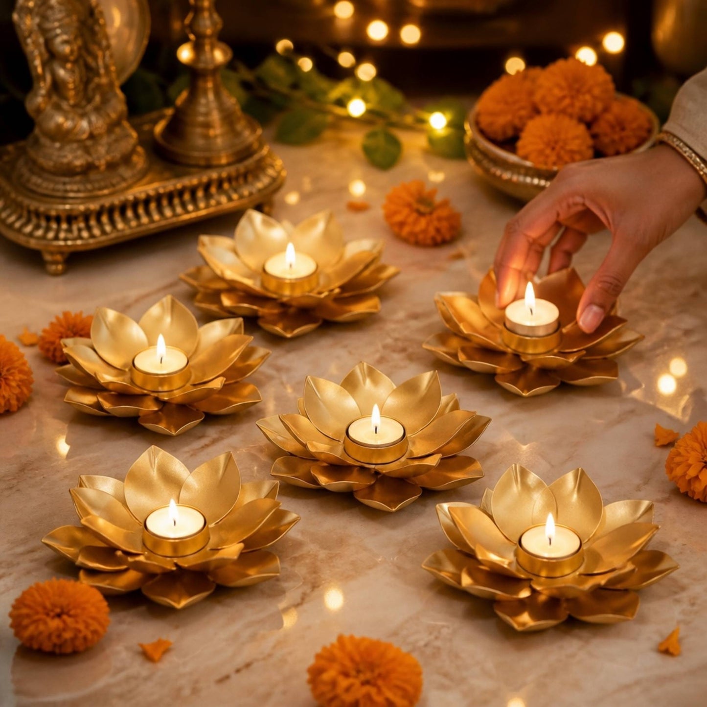 Six gold lotus t-light holders lit near a brass idol and marigolds on a marble floor
