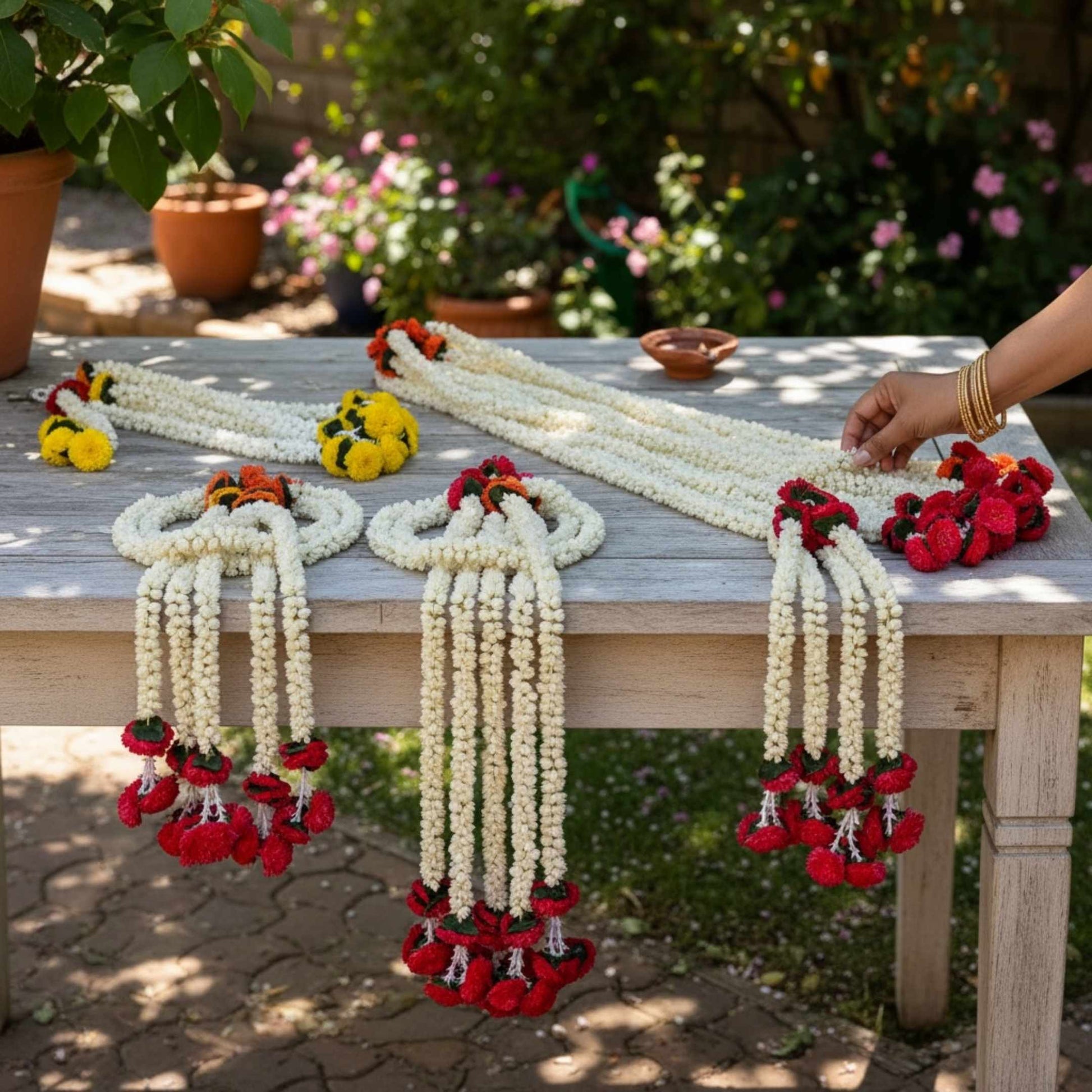 Decorative garlands on a table outdoors with a person's hand interacting with them.