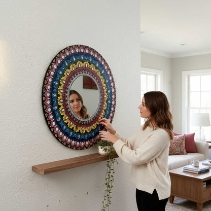Woman adjusting a colorful round mandal mirror in a living room.