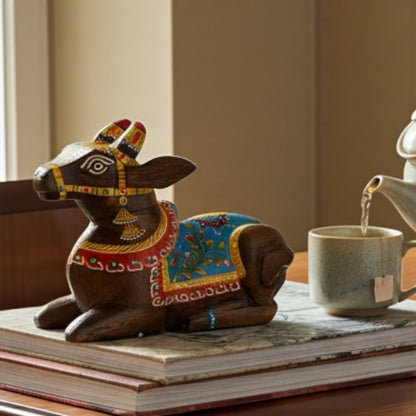 Decorative wooden cow figurine with colorful patterns on a table next to a teacup.