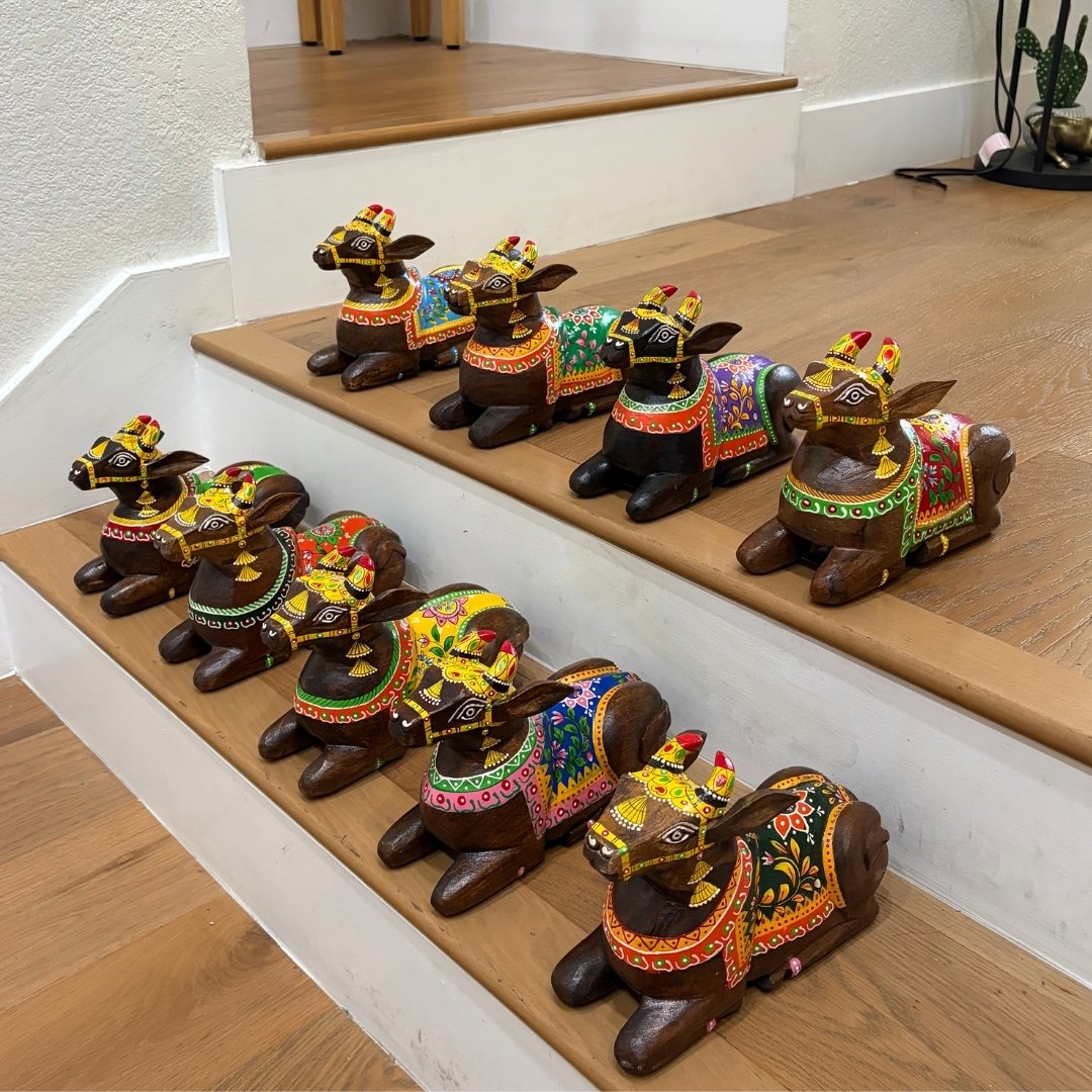 Multiple 9-inch hand-painted mango-wood Nandi figurines in different color variants, displayed together  on a wooden staircase.