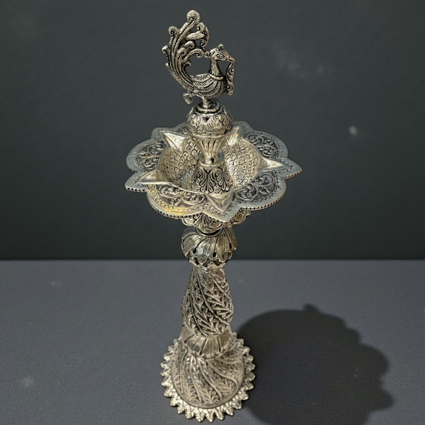 close-up of peacock engraving and antique silver finish on Nilavilakku traditional oil lamp
