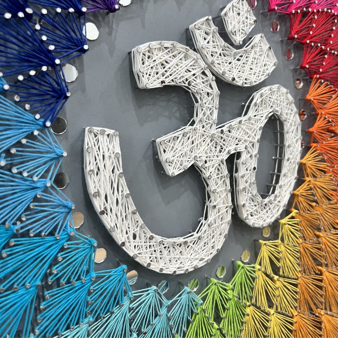 Detailed view of the sacred Om symbol meticulously outlined with nails and filled with intricate colorful string art patterns.