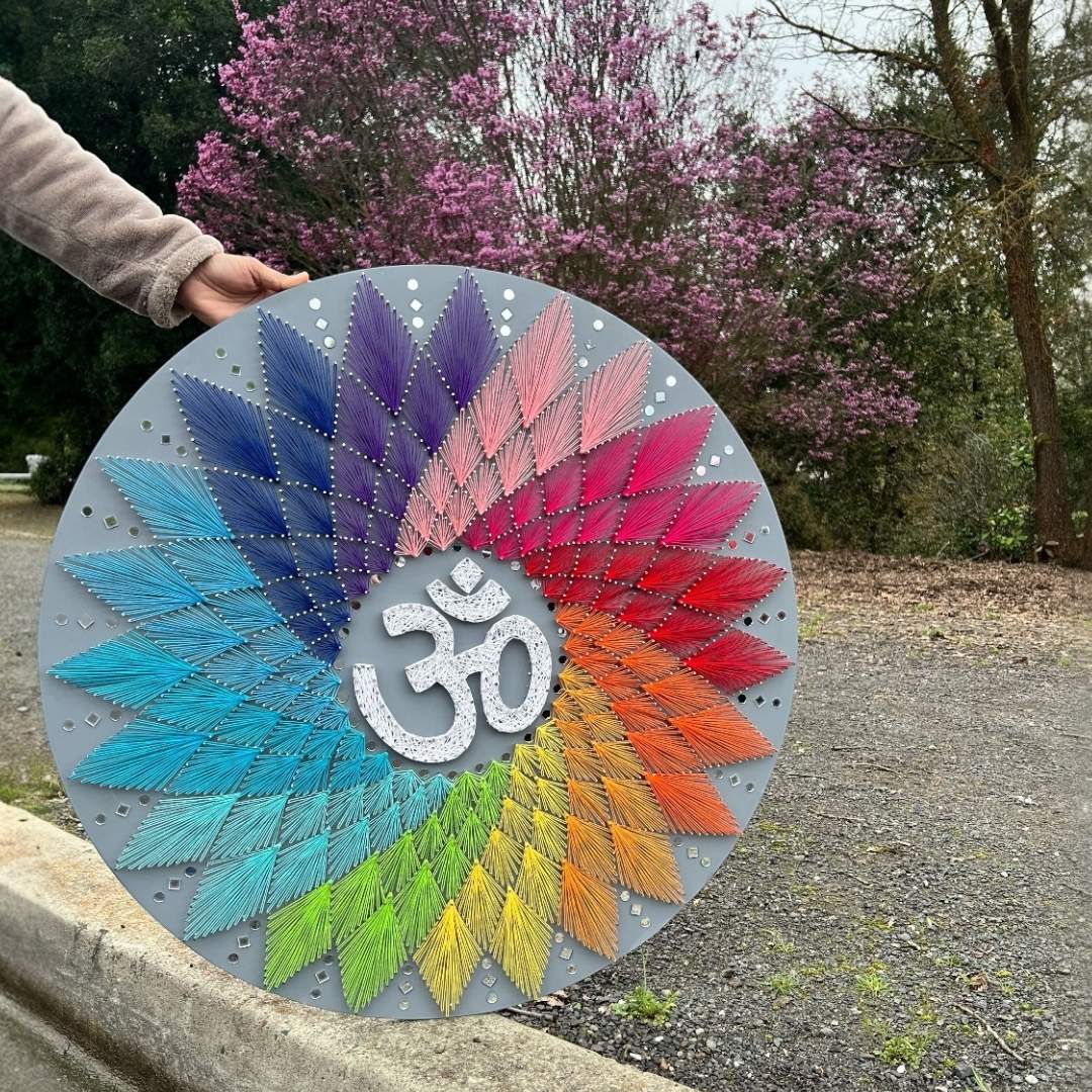 Colorful circular art piece with Om symbol held outdoors against a natural background
