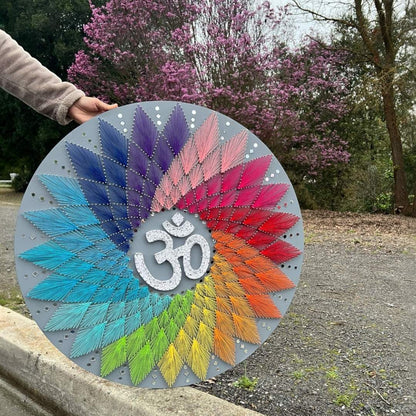 Colorful circular art piece with Om symbol held outdoors against a natural background