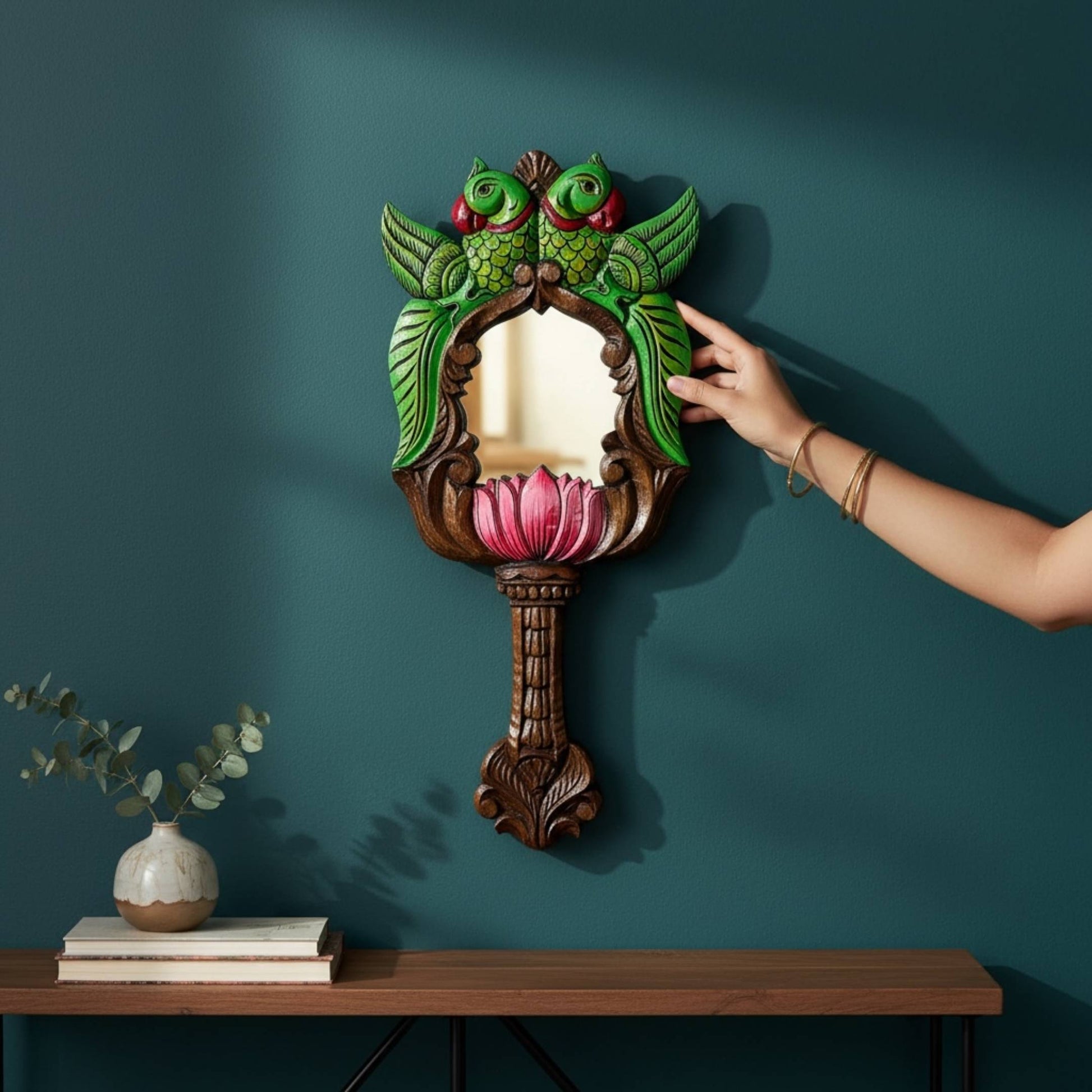 Hand-painted green parrot lotus wall mirror on dark teal wall – South Indian carved wood decor