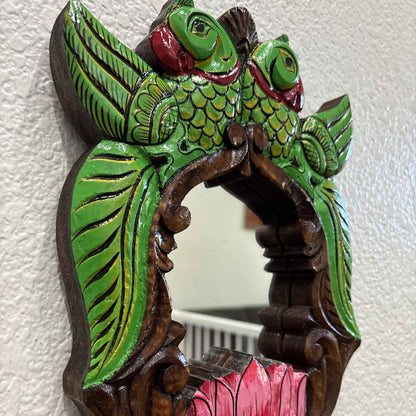 Close-up: hand-carved green parrots with red beaks and pink lotus on South Indian wooden mirror