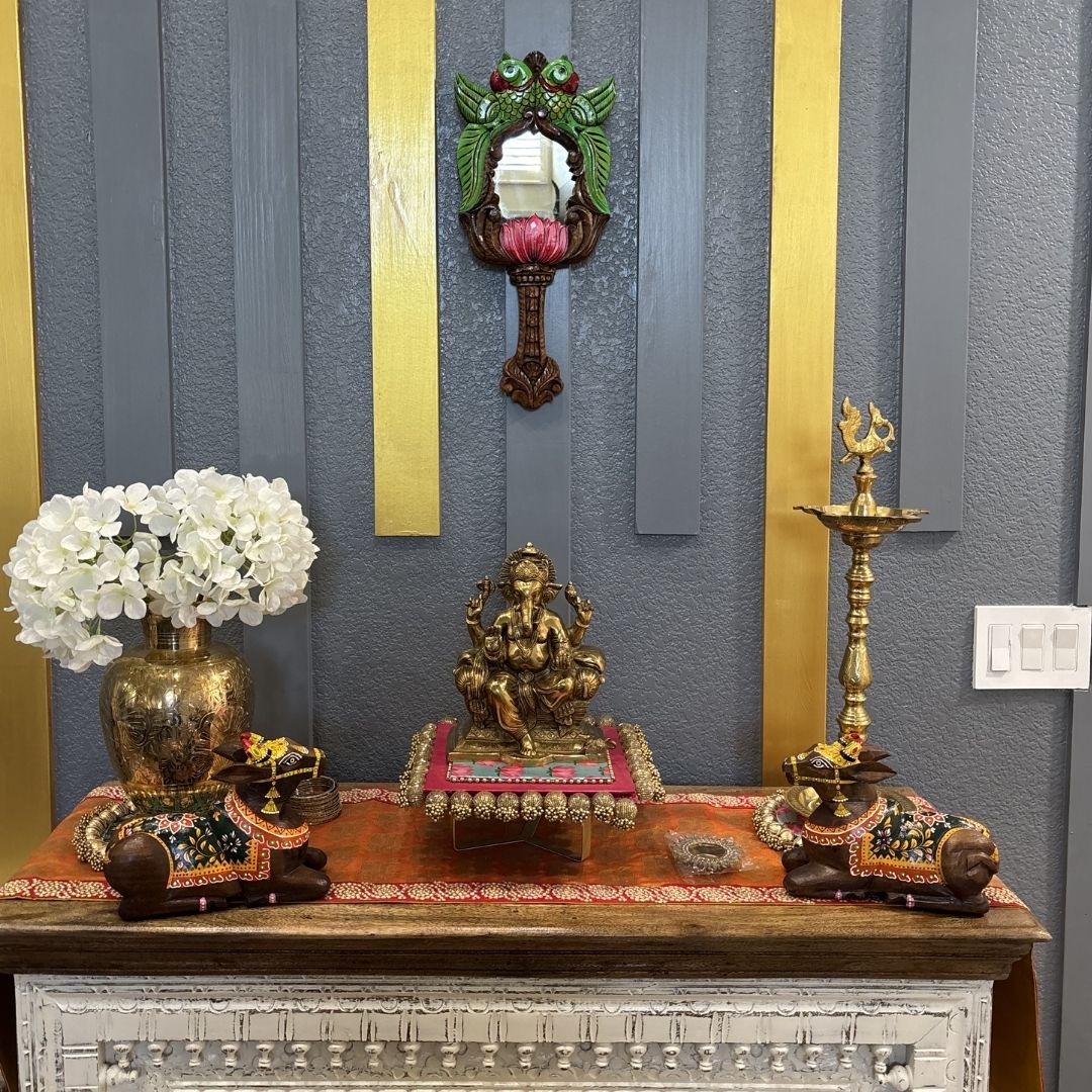 South Indian parrot lotus mirror above Ganesha statue and brass lamps – puja room wall decor