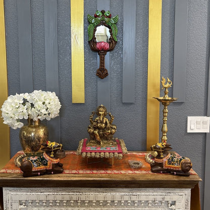 South Indian parrot lotus mirror above Ganesha statue and brass lamps – puja room wall decor