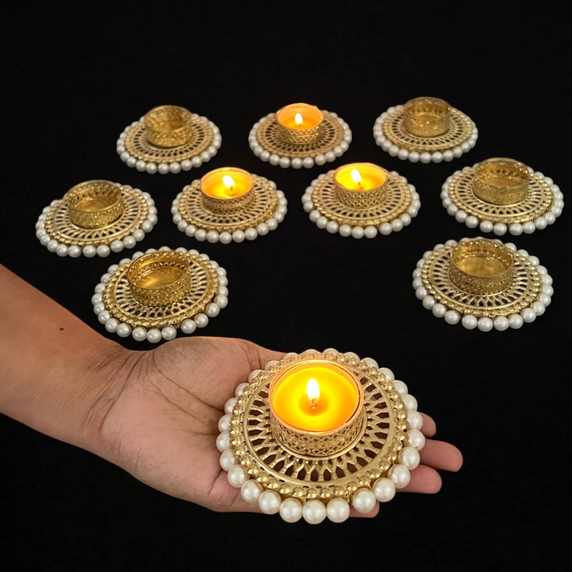 Decorative candles with gold and pearl design held by a hand against a black background