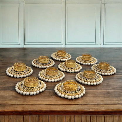 Set of gold t-light with white bead borders on a wooden surface.