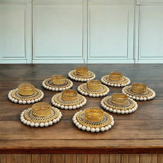 Set of gold t-light with white bead borders on a wooden surface.