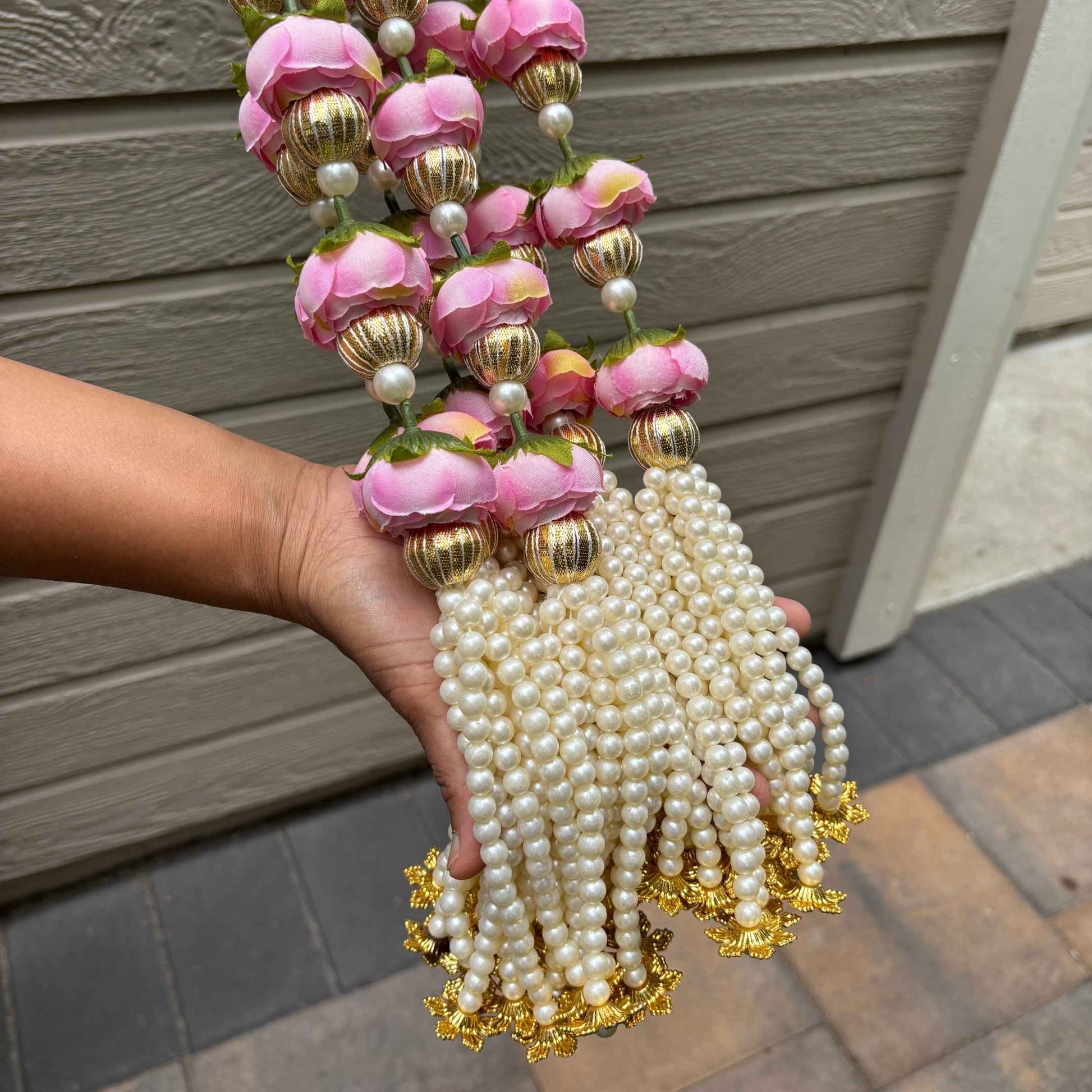 Decorative tassel with pink flowers, pearls, and gold accents held by a hand against a wooden background.