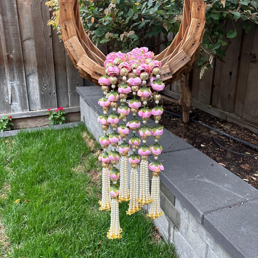 Decorative hanging with pink a flowers on a grassy area with a wooden fence in the background.